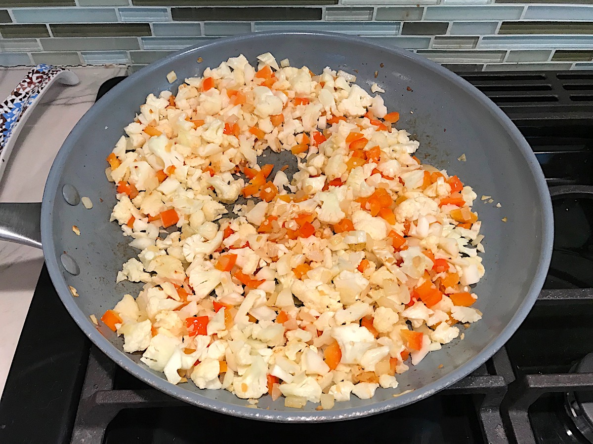 Cauliflower pieces added to diced red pepper, onions, and minced garlic in a frying pan cooking for the Vegetarian Sloppy Joes recipe.