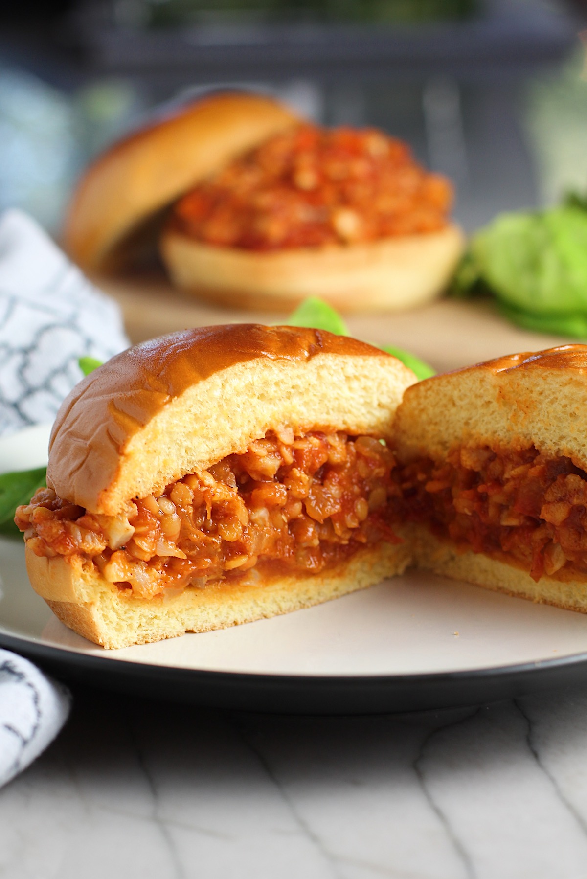 Vegetarian Sloppy Joes sandwich overstuffed with cauliflower and lentils filling in a brioche bun on a plate cut in half and facing out to see the center.