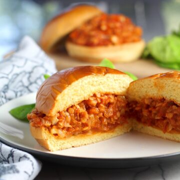 Vegetarian Sloppy Joes sandwich overstuffed with cauliflower and lentils filling in a brioche bun on a plate cut in half and facing out to see the center.