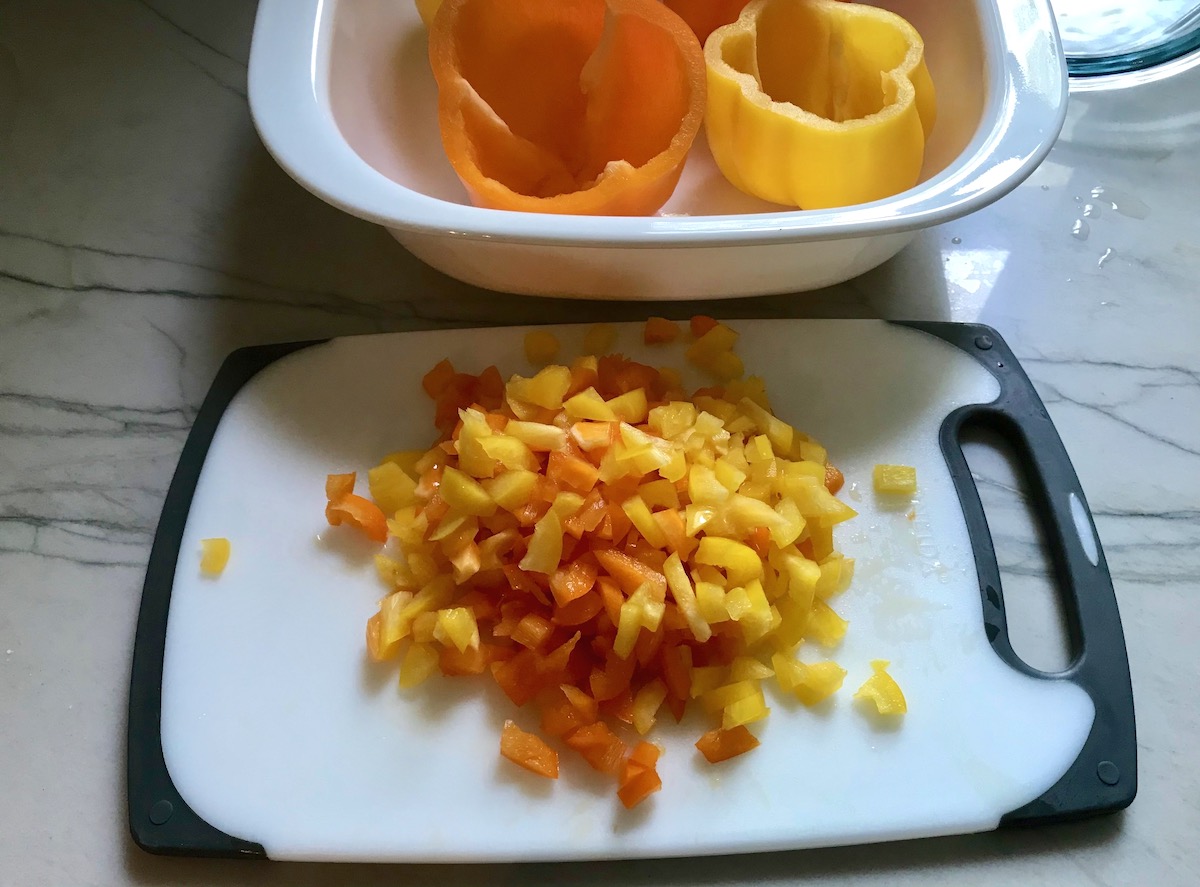 Tops of bell peppers diced on a cutting board in front of dish with hollowed out yellow and orange bell peppers for Stuffed Peppers without Rice.