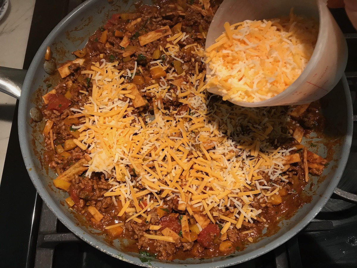 Shredded cheese being added to skillet with Tex Mex ground beef filling for the Stuffed Peppers without Rice recipe.