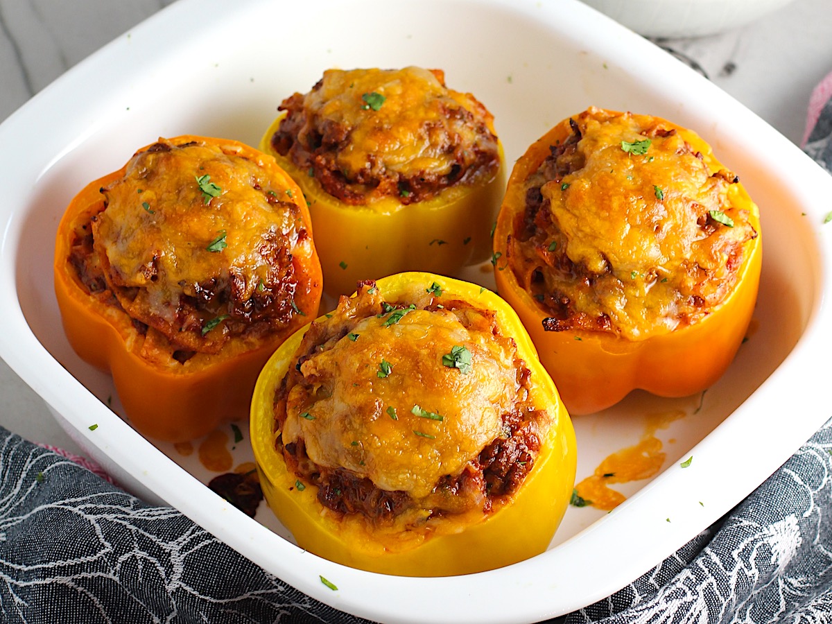 Four Tex Mex Beef Stuffed Peppers without Rice, but covered in melted cheese in a white casserole dish. Everything is set on the counter with a towel in front.
