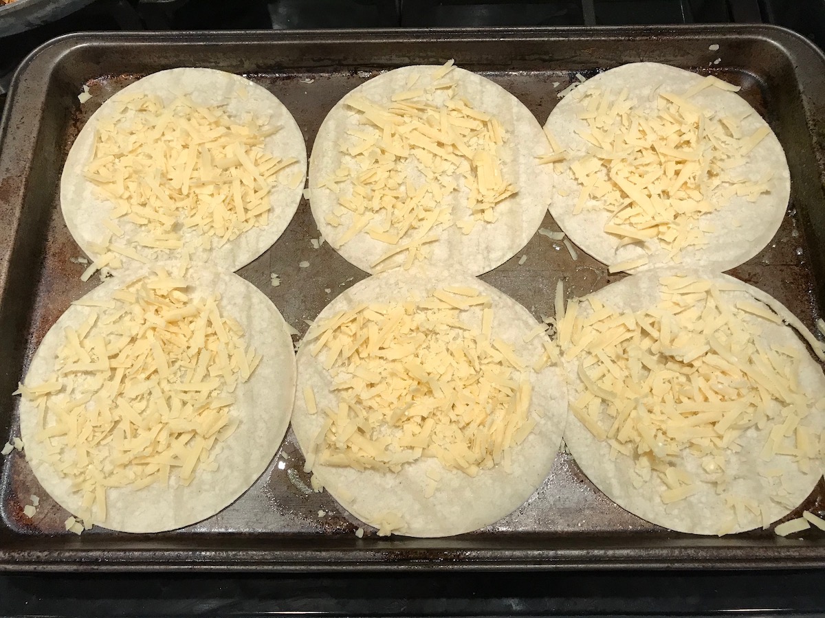Shredded white cheddar cheese on 6 flat corn tortillas before cooking Rotisserie Chicken Quesadillas recipe.