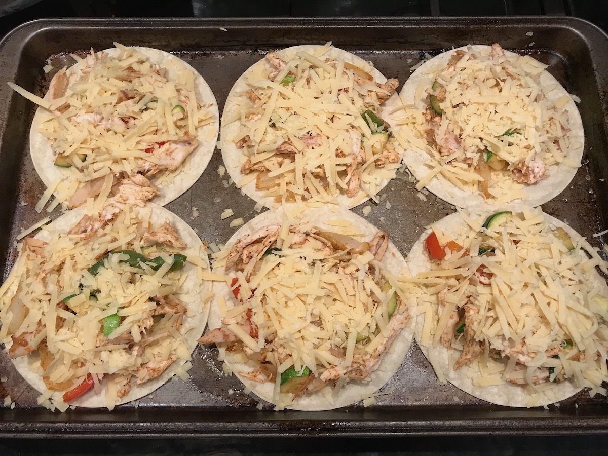 More shredded cheese added on top of cooked shredded chicken, onions, red peppers, and zucchini on 6 flat corn tortillas before cooking these Rotisserie Chicken Quesadillas recipe.