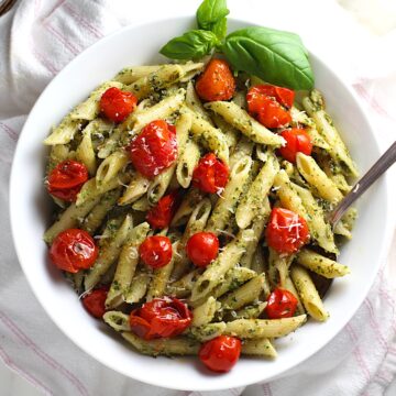 Penne pasta coated with pesto, topped with roasted cherry tomatoes, parmesan sprinkled on top and fresh basil leaves on the side of the bowl. This Pesto Pasta with tomatoes recipe is an easy dinner.