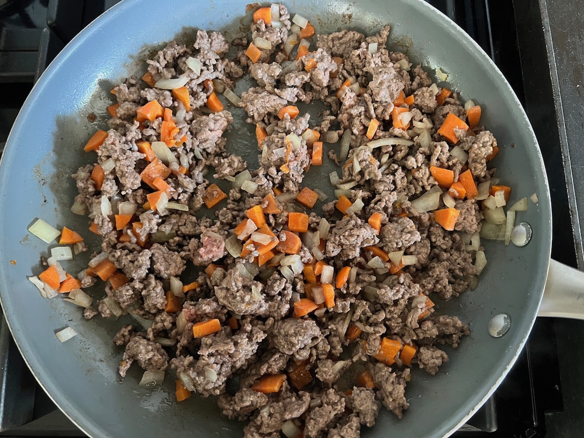Ground beef, carrots, onions, and garlic cooking in a skillet for Ground Beef and Zucchini Casserole recipe.
