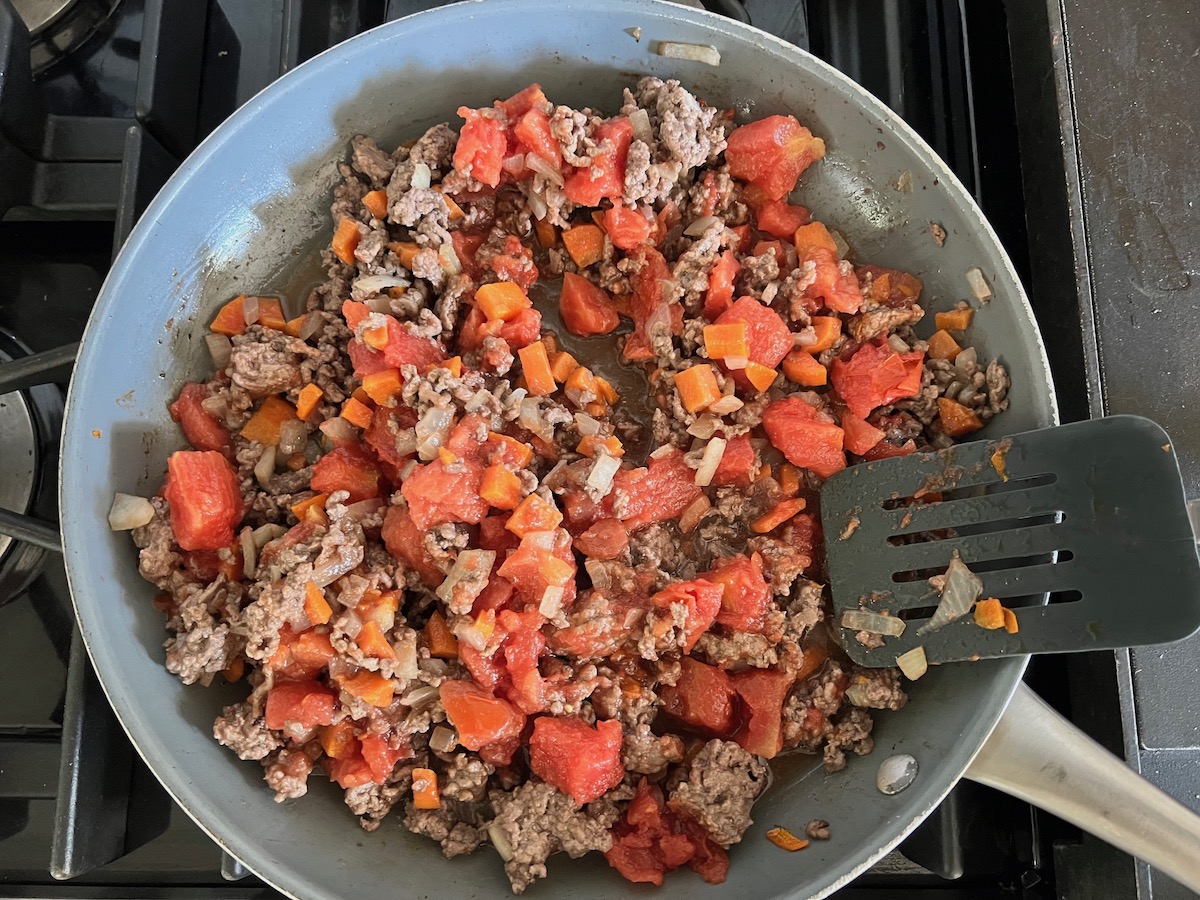 Dice Tomatoes added to ground beef mixture cooking in a skillet for Ground Beef and Zucchini Casserole recipe.