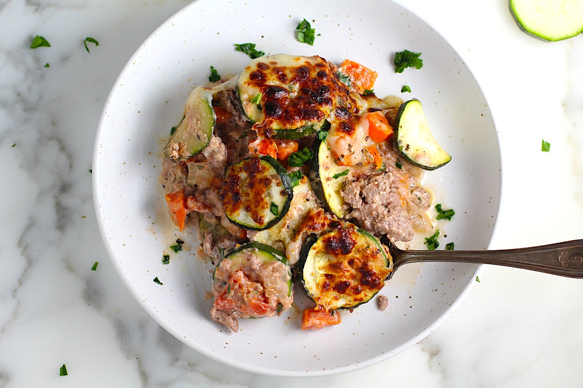 Ground Beef and Zucchini Casserole baked golden brown on a plate with fork and parsley sprinkled on top.
