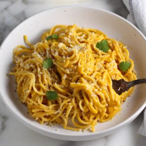 Creamy Butternut Squash Spaghetti on a plate on counter with fork and fresh parsley garnish on top.