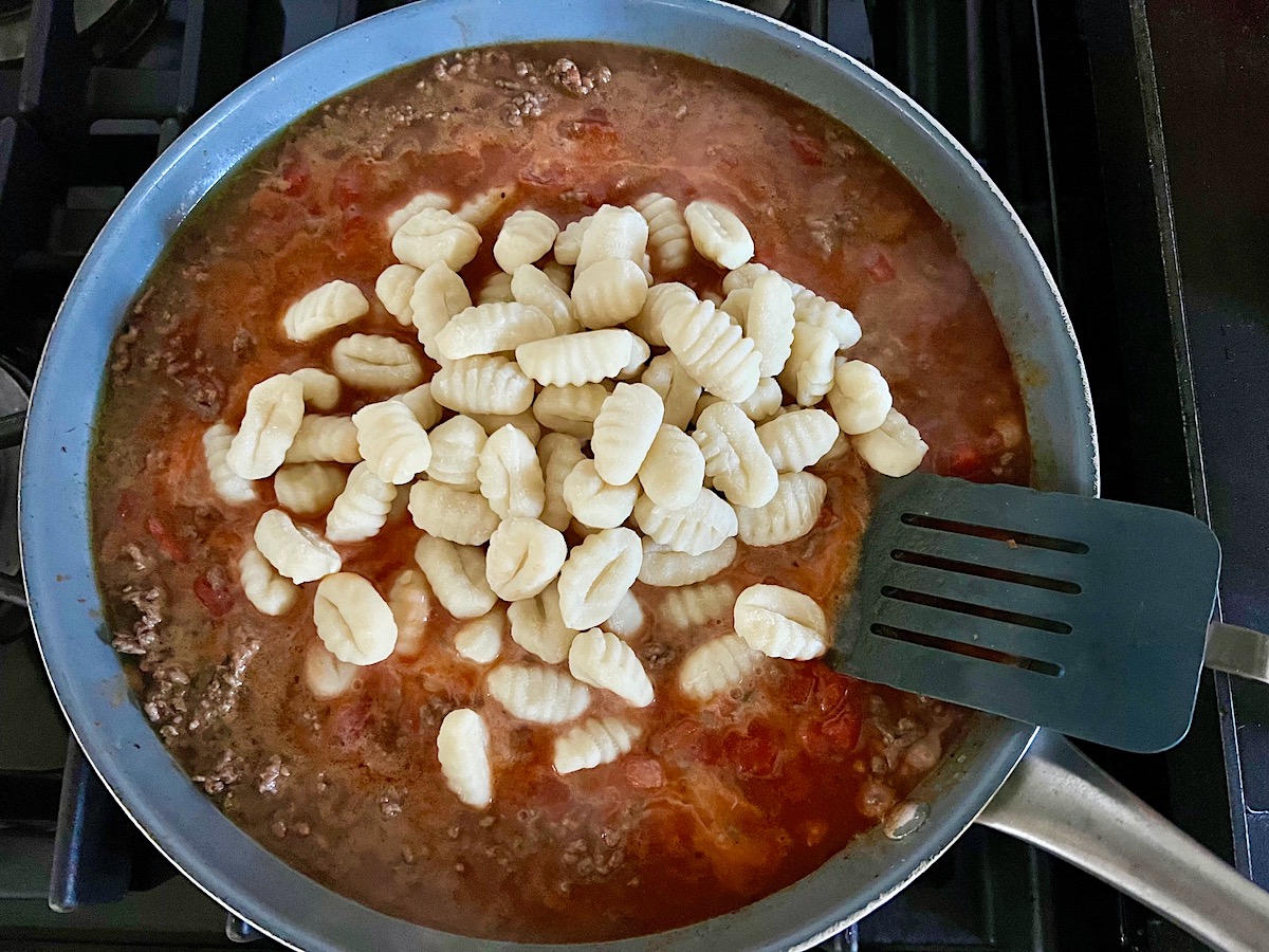 Uncooked gnocchi added to ground beef sauce in a skillet on the stove for Ground Beef Gnocchi skillet recipe.