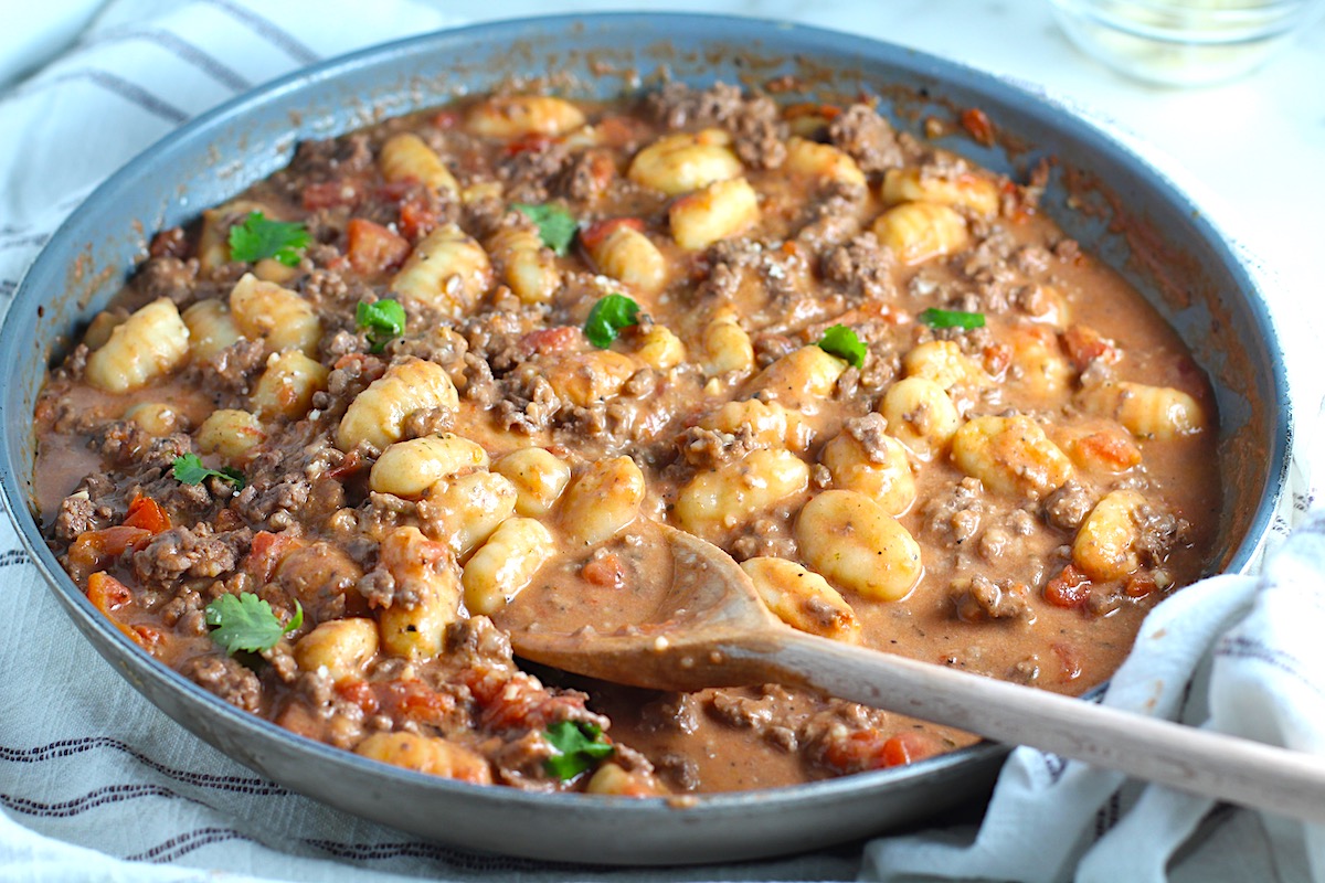 Ground Beef Gnocchi Skillet recipe on a plate with fresh parsley garnish in a skillet with a wood spatula.