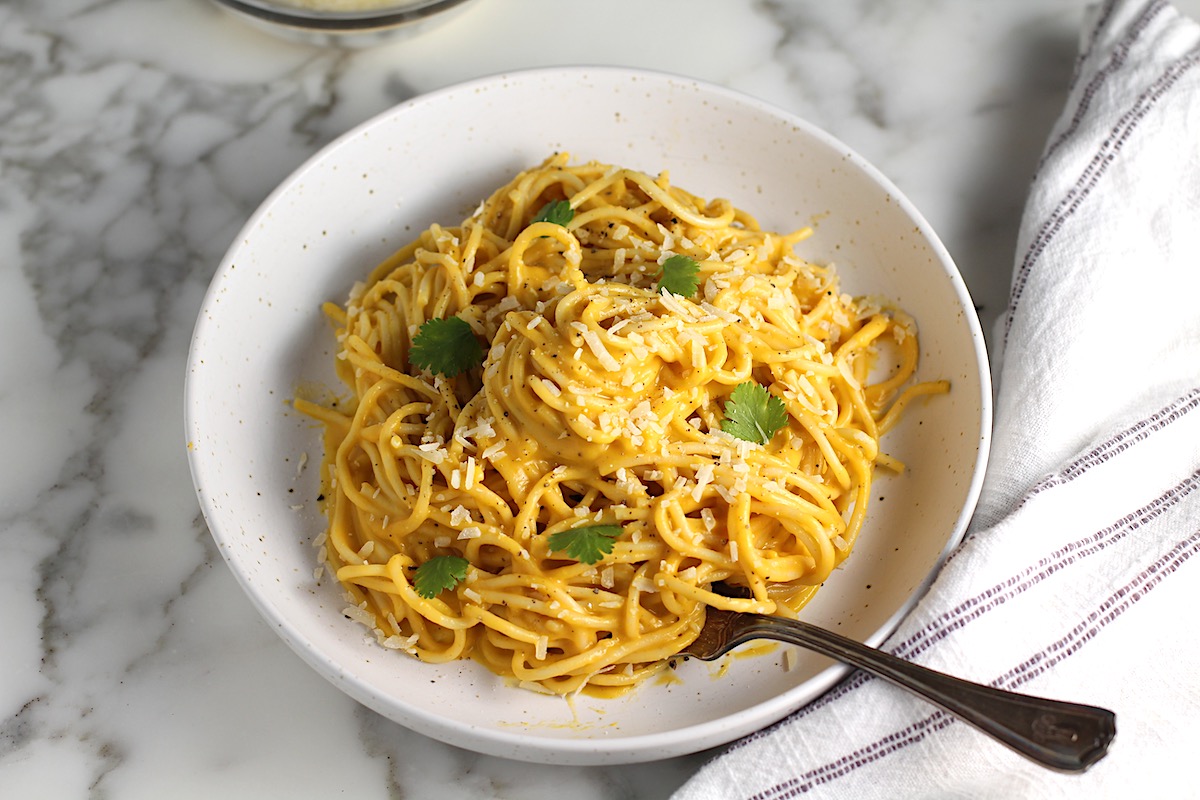 Creamy Butternut Squash Spaghetti on a plate on counter with fork and fresh parsley garnish on top.