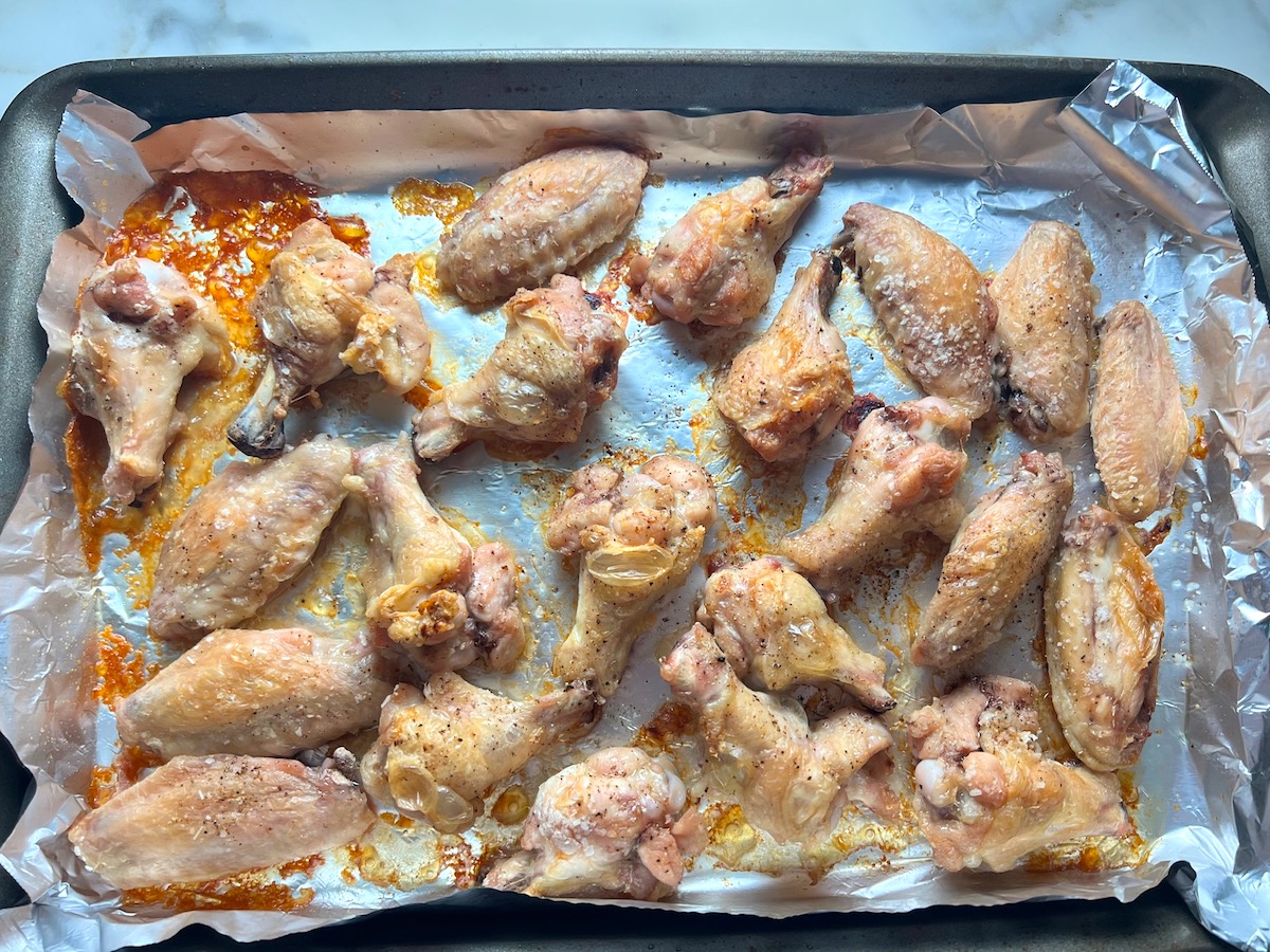 Cooked chicken wings and drumettes on a foil-lined sheet pan for the Apricot Sauce Wings recipe.