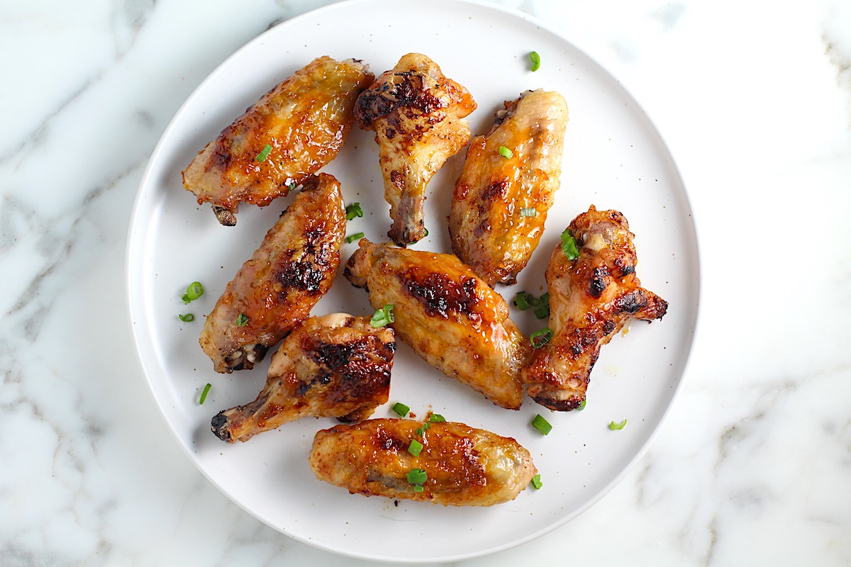 Sticky Garlic Soy Apricot Sauce Wings on a plate with scallion slices sprinkled on top.