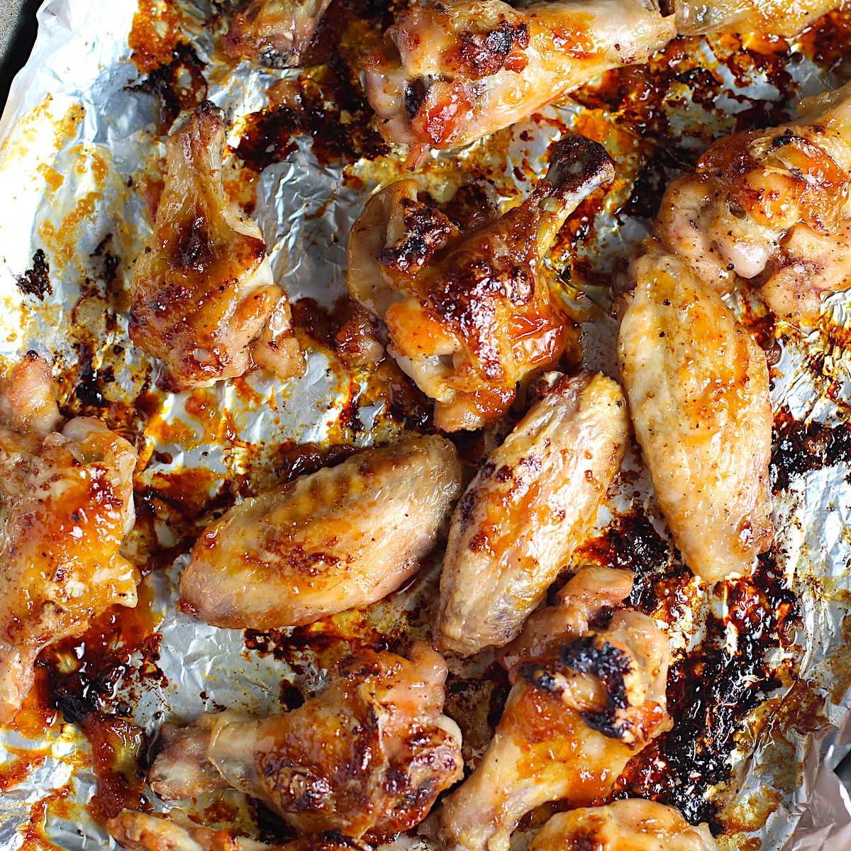 Cooked and slightly charred Sticky Garlic Soy Apricot Sauce Wings on a foil-lined sheet pan.