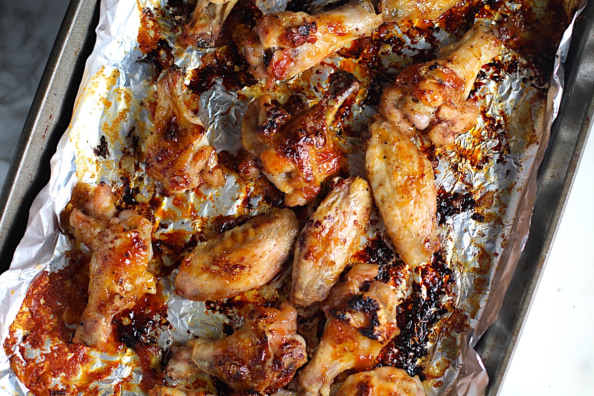 Cooked and slightly charred Sticky Garlic Soy Apricot Sauce Wings on a foil-lined sheet pan.