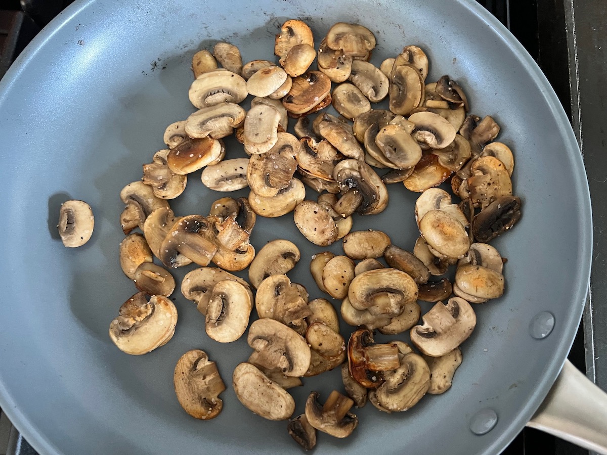 Mushrooms sauteeing in a large frying pan on the stove for Mushroom Alfredo Fettuccine pasta.