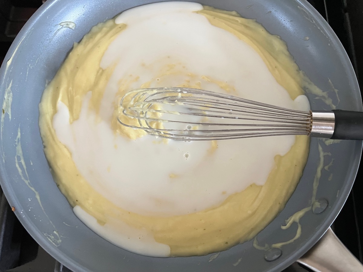 Milk being whisked into the alfredo sauce in a large frying pan on the stove for Mushroom Alfredo Fettuccine pasta.