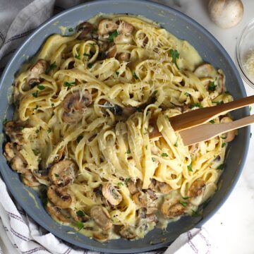 Mushroom Alfredo Fettuccine pasta in a pan with wooden tongs scooping up pasta.